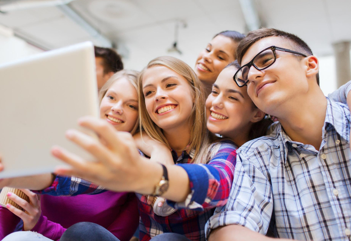 Na zdjęciu grupa młodych, uśmiechniętych ludzi patrzących w laptop.