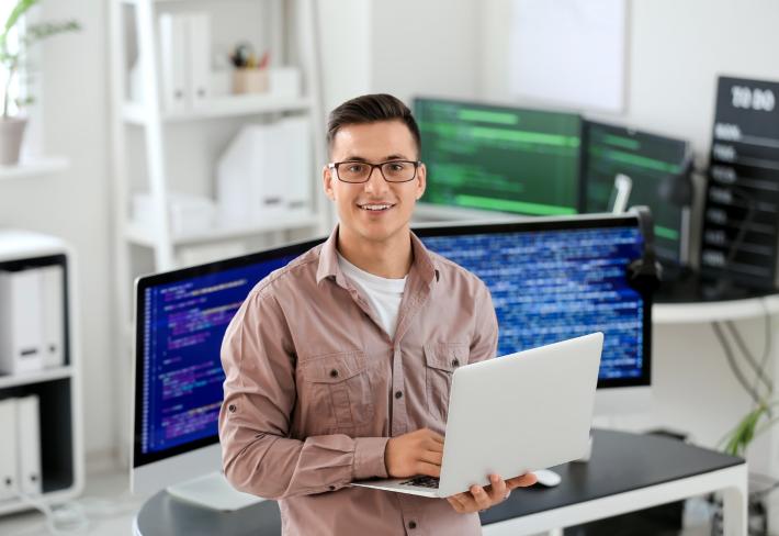 Na zdjęciu młody człowiek, informatyk z laptopem z ręku